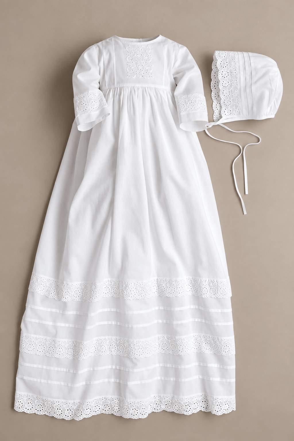 A white baby girl's christening gown with matching bonnet, laid flat on a beige background. The nightgown features long sleeves with lace cuffs, a smocked chest, and lace trim at the hem, accompanied by a matching bonnet with lace trim and tie strings.