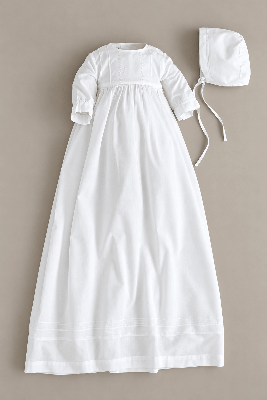 A white long-sleeve baby christening dress with a smocked bodice and a matching white bonnet, laid flat on a neutral beige background.